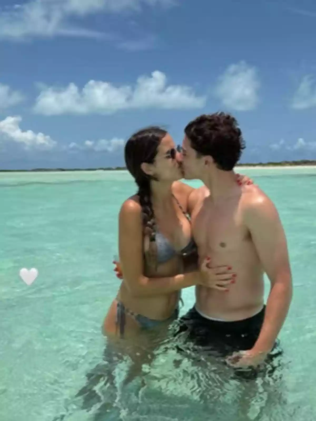 Young couple kissing in the sea with crystal-clear water and a blue sky in the background Young couple kissing in the sea with crystal-clear water and a blue sky in the background