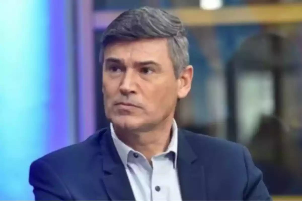Gray-haired, short-haired man wearing a blue blazer and light-colored jersey looking to the side in a studio or television set environment Gray-haired, short-haired man wearing a blue blazer and light-colored jersey looking to the side in a studio or television set environment