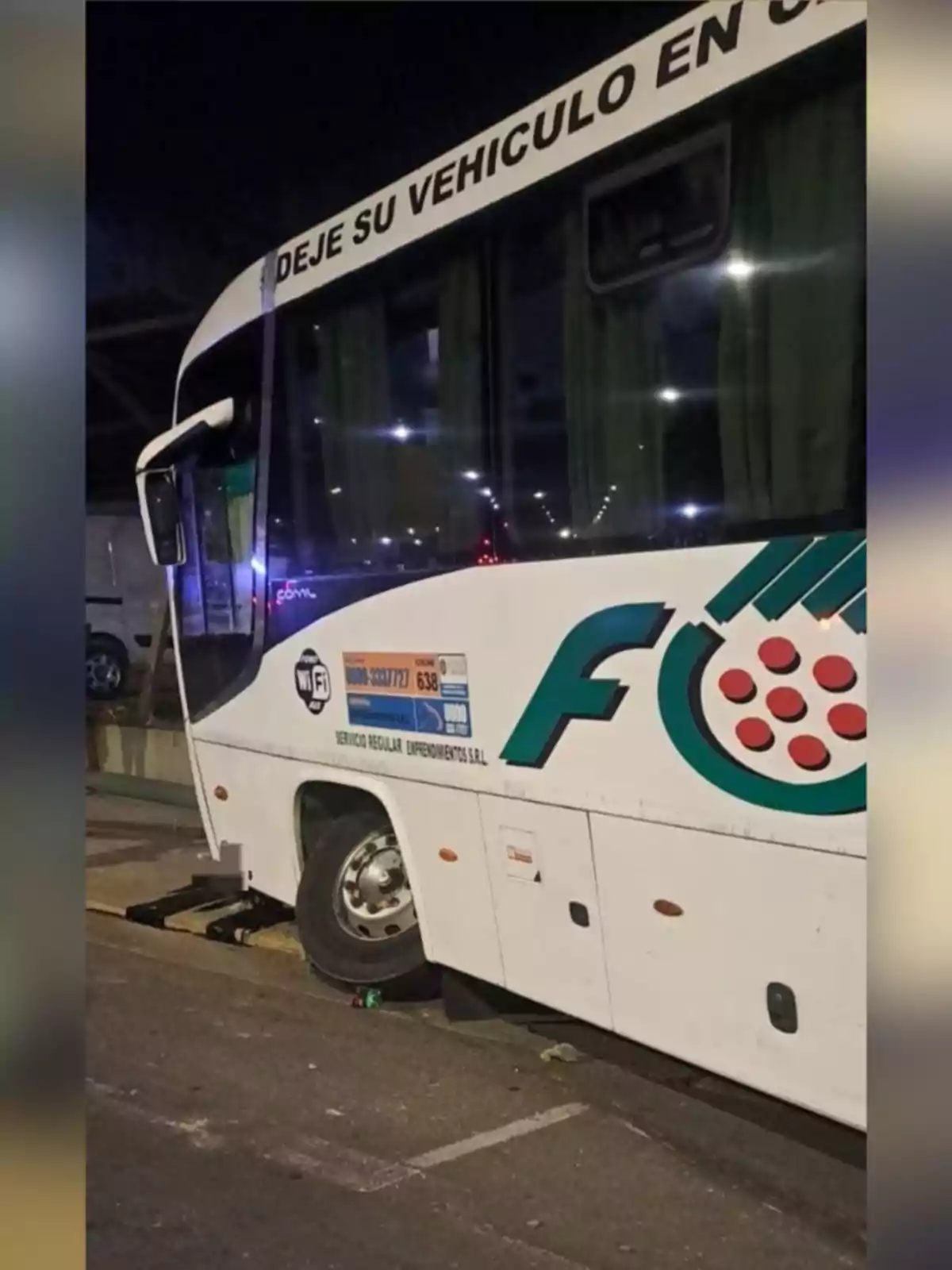 White bus parked with its front left tire on a curb, partially sunk into a ditch, at night. White bus parked with its front left tire on a curb, partially sunk into a ditch, at night.