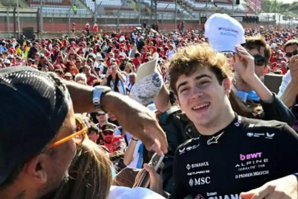 Joven con uniforme de automovilismo sonriendo y firmando autógrafos entre una multitud en un evento deportivo