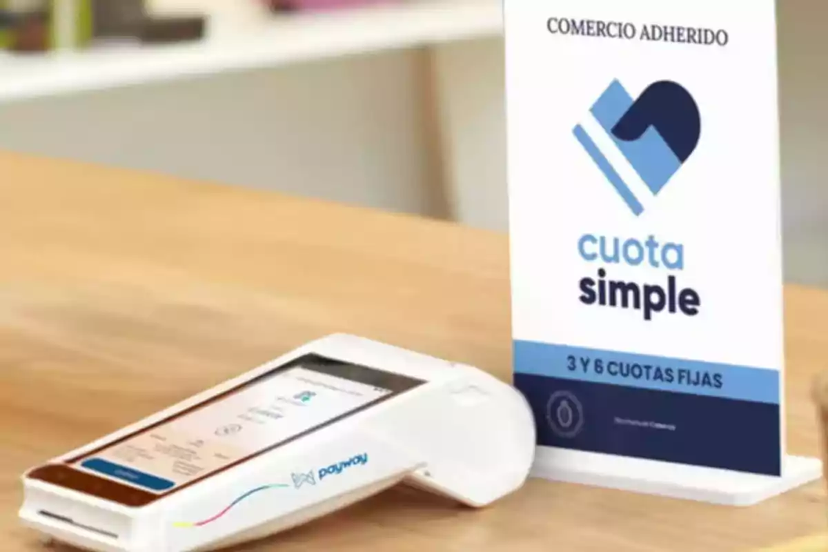 Terminal de pago electrónica sobre una mesa junto a un cartel de cuota simple que indica la posibilidad de pagar en 3 y 6 cuotas fijas Terminal de pago electrónica sobre una mesa junto a un cartel de cuota simple que indica la posibilidad de pagar en 3 y 6 cuotas fijas
