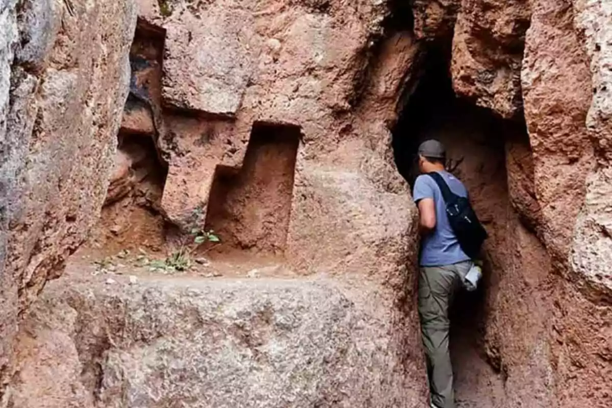 Persona entrando a una cueva en una formación rocosa con un escalón tallado en la piedra Persona entrando a una cueva en una formación rocosa con un escalón tallado en la piedra