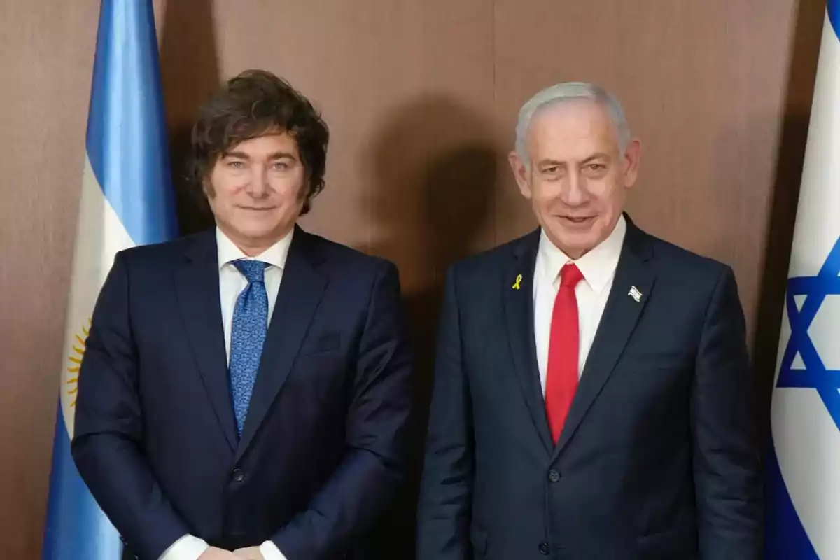 Two men in suits pose together in front of the flags of Argentina and Israel. Two men in suits pose together in front of the flags of Argentina and Israel.