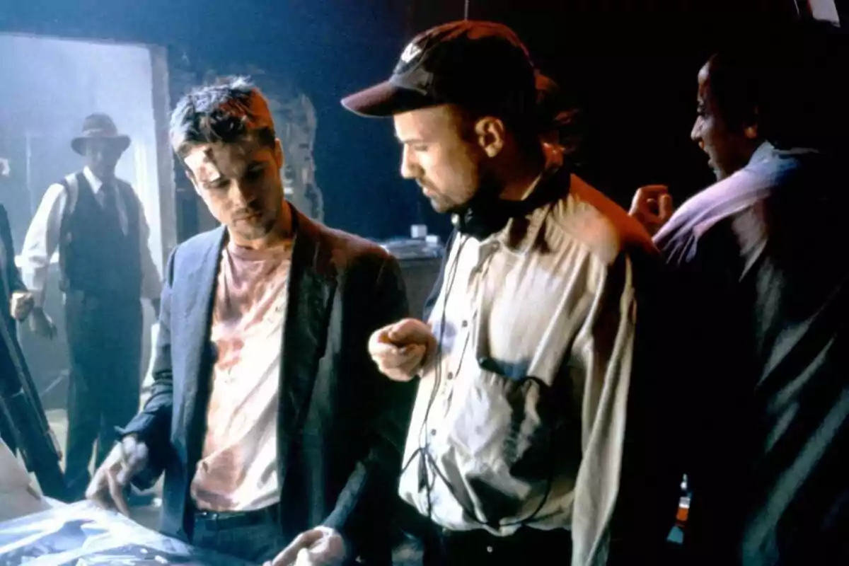 Dos hombres conversan en un set de filmación mientras otros observan al fondo Dos hombres conversan en un set de filmación mientras otros observan al fondo