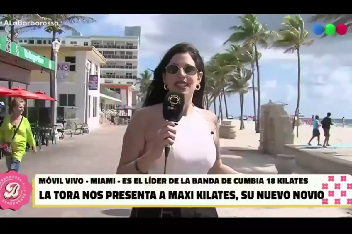 Reportera con gafas de sol y micrófono en la mano transmitiendo en vivo desde una playa de Miami con palmeras y personas de fondo, junto a un cintillo informativo sobre una banda de cumbia y un nuevo novio Reportera con gafas de sol y micrófono en la mano transmitiendo en vivo desde una playa de Miami con palmeras y personas de fondo, junto a un cintillo informativo sobre una banda de cumbia y un nuevo novio