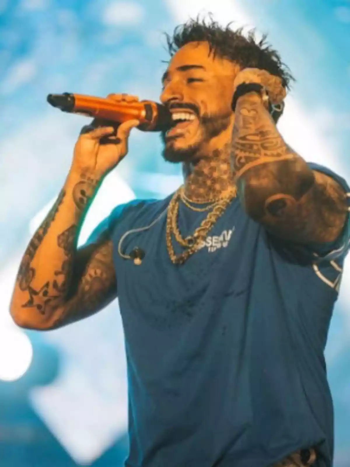 Hombre tatuado cantando en un escenario con micrófono naranja y camiseta azul Hombre tatuado cantando en un escenario con micrófono naranja y camiseta azul