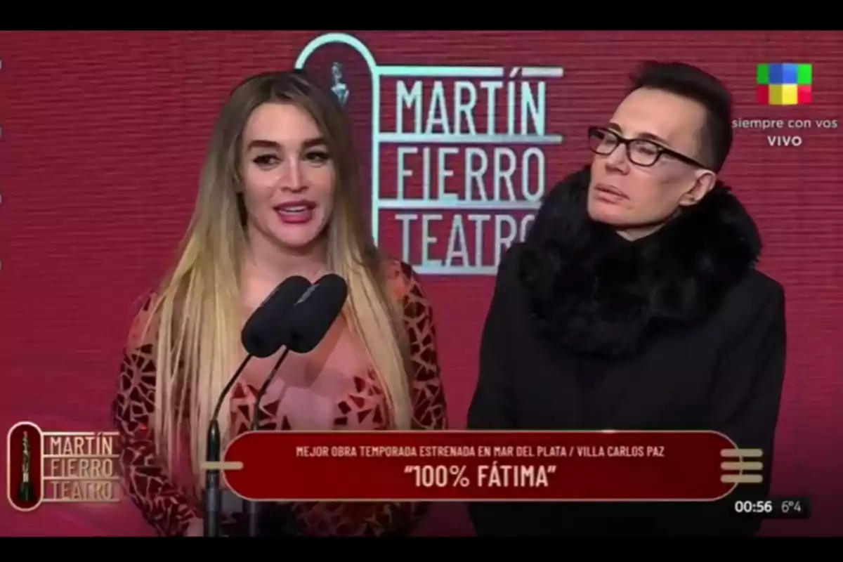 Two people on stage during the Martín Fierro Theater Awards ceremony with a red background and the event’s logo; one of them is speaking into the microphones, and the screen announces that the winning play is 100% Fátima. Two people on stage during the Martín Fierro Theater Awards ceremony with a red background and the event’s logo; one of them is speaking into the microphones, and the screen announces that the winning play is 100% Fátima.