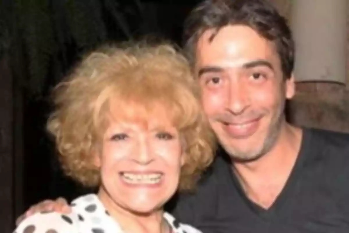 Dos personas sonríen y posan juntas para una foto en un ambiente interior.