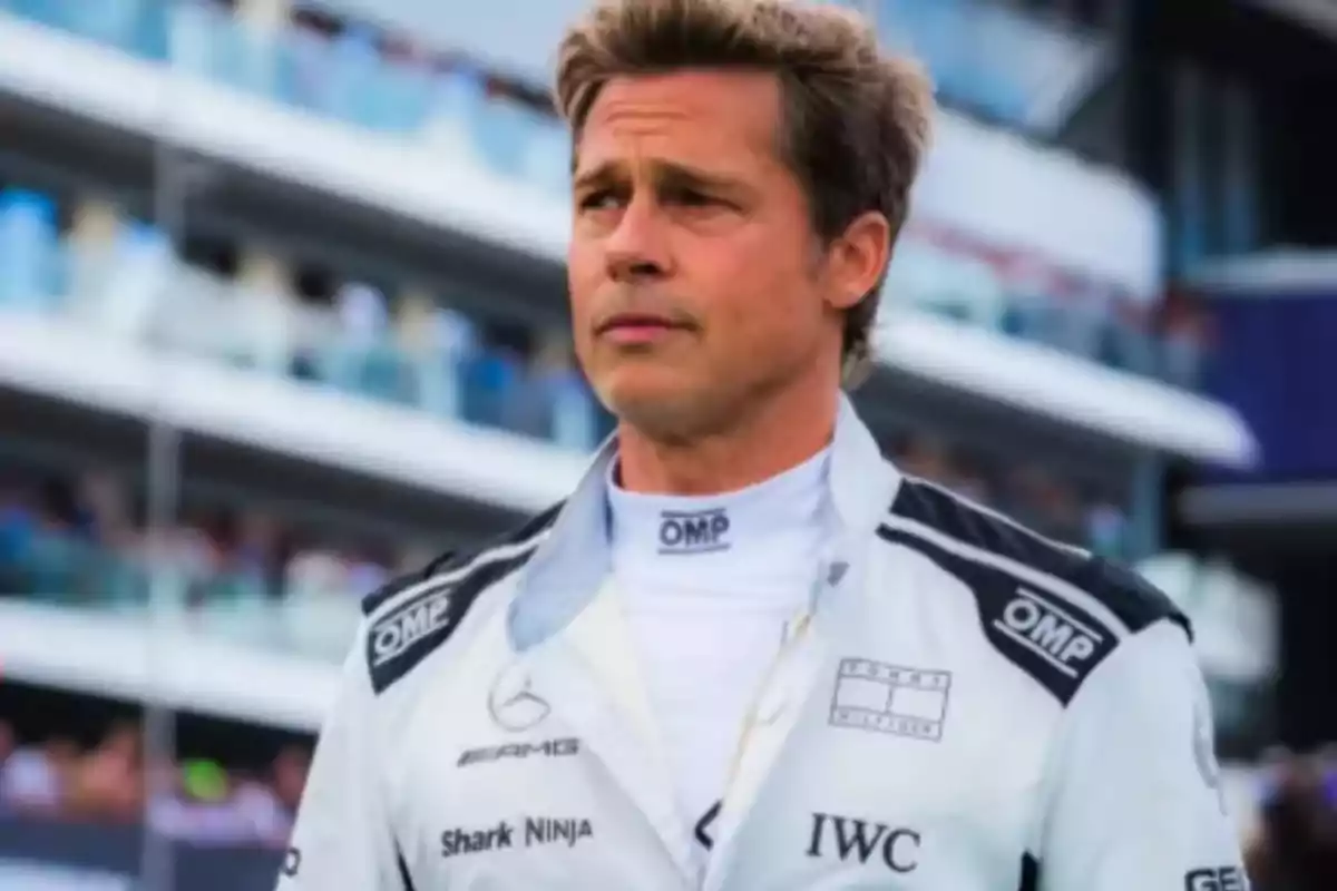 Man in a racing driver's suit on a track with grandstands in the background