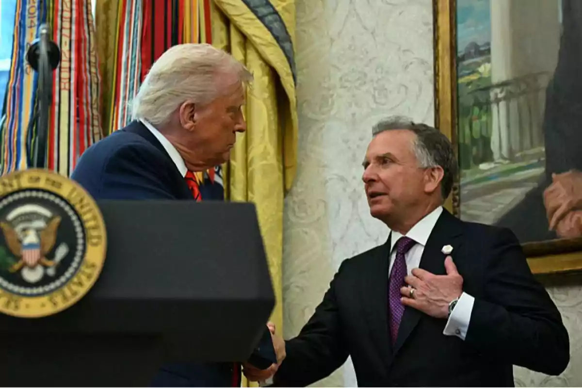 Two men in suits shake hands in an official office with flags and a presidential podium at the front. Two men in suits shake hands in an official office with flags and a presidential podium at the front.