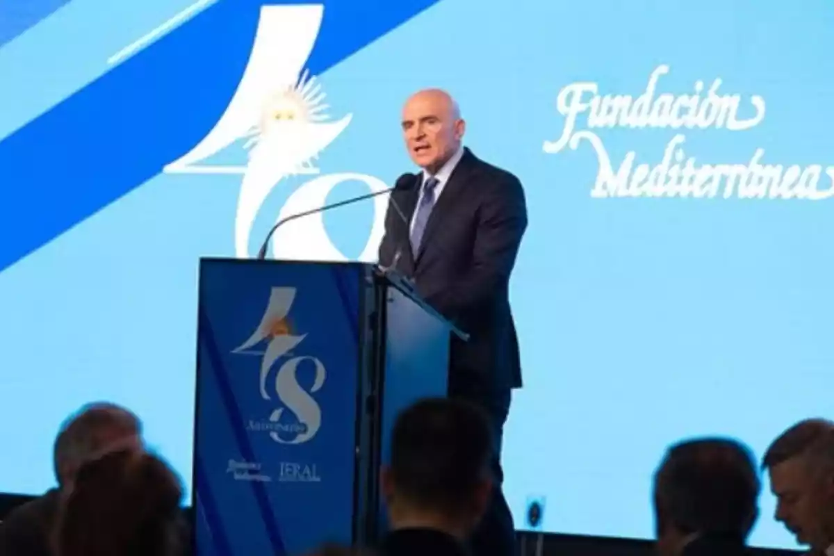 Hombre calvo con traje hablando en un podio durante un evento de la Fundación Mediterránea con fondo azul y logotipo de 40 aniversario.