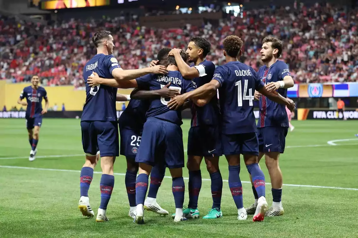 PSG players celebrate a goal by hugging on the field during a soccer match with a stadium full of fans in the background. PSG players celebrate a goal by hugging on the field during a soccer match with a stadium full of fans in the background.