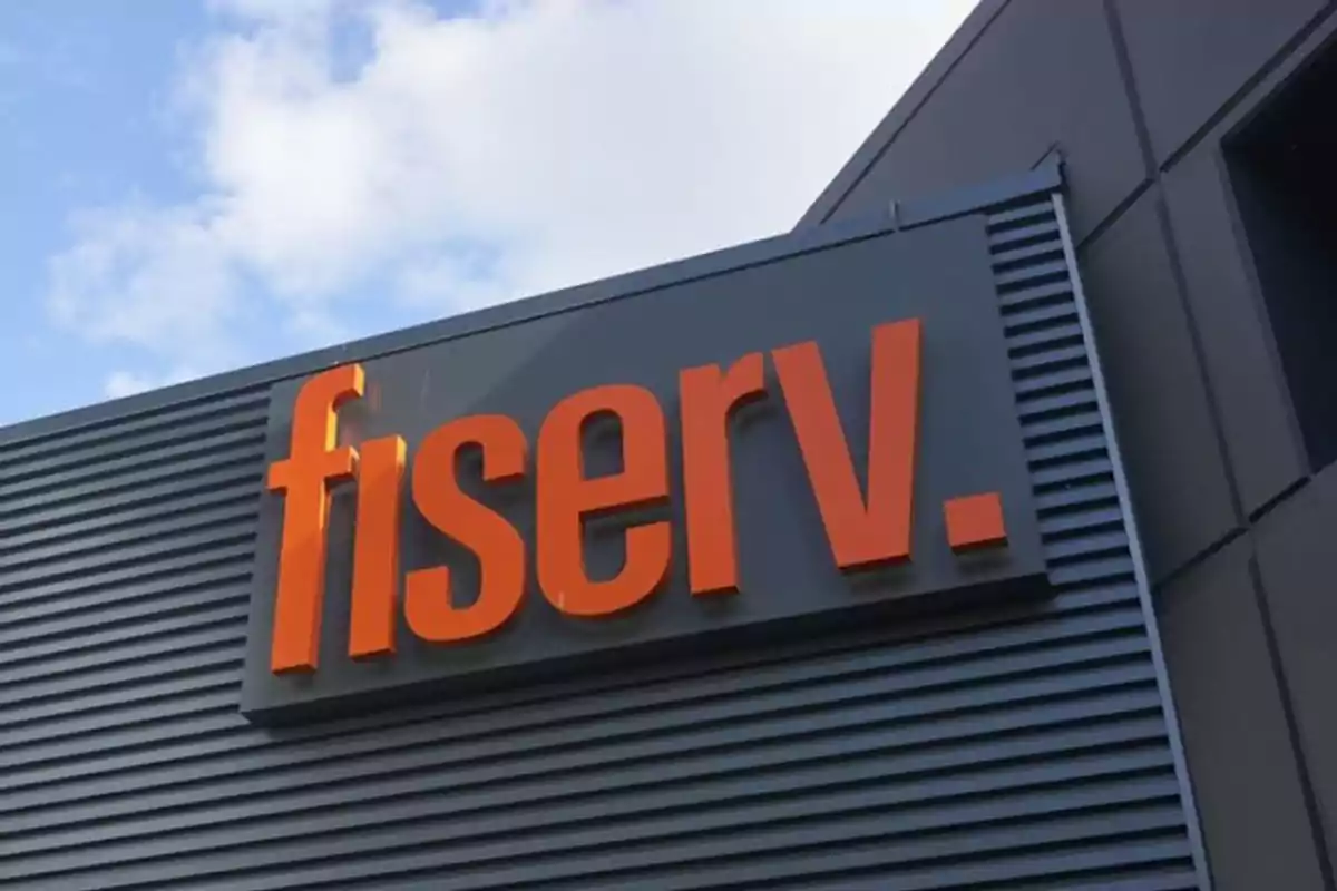Letrero de la empresa Fiserv en la fachada de un edificio moderno bajo un cielo parcialmente nublado Letrero de la empresa Fiserv en la fachada de un edificio moderno bajo un cielo parcialmente nublado