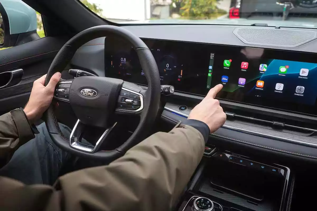 Persona manejando un auto Ford mientras interactúa con la pantalla táctil del sistema de infoentretenimiento Persona manejando un auto Ford mientras interactúa con la pantalla táctil del sistema de infoentretenimiento