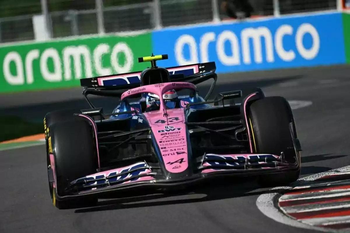 Un monoplaza de Fórmula 1 color rosa y azul toma una curva en un circuito con publicidad de Aramco al fondo
