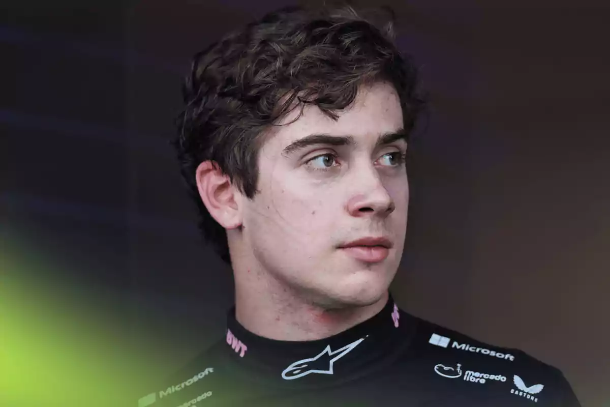 Young man with curly hair and a serious expression wearing a black racing suit with sponsor logos