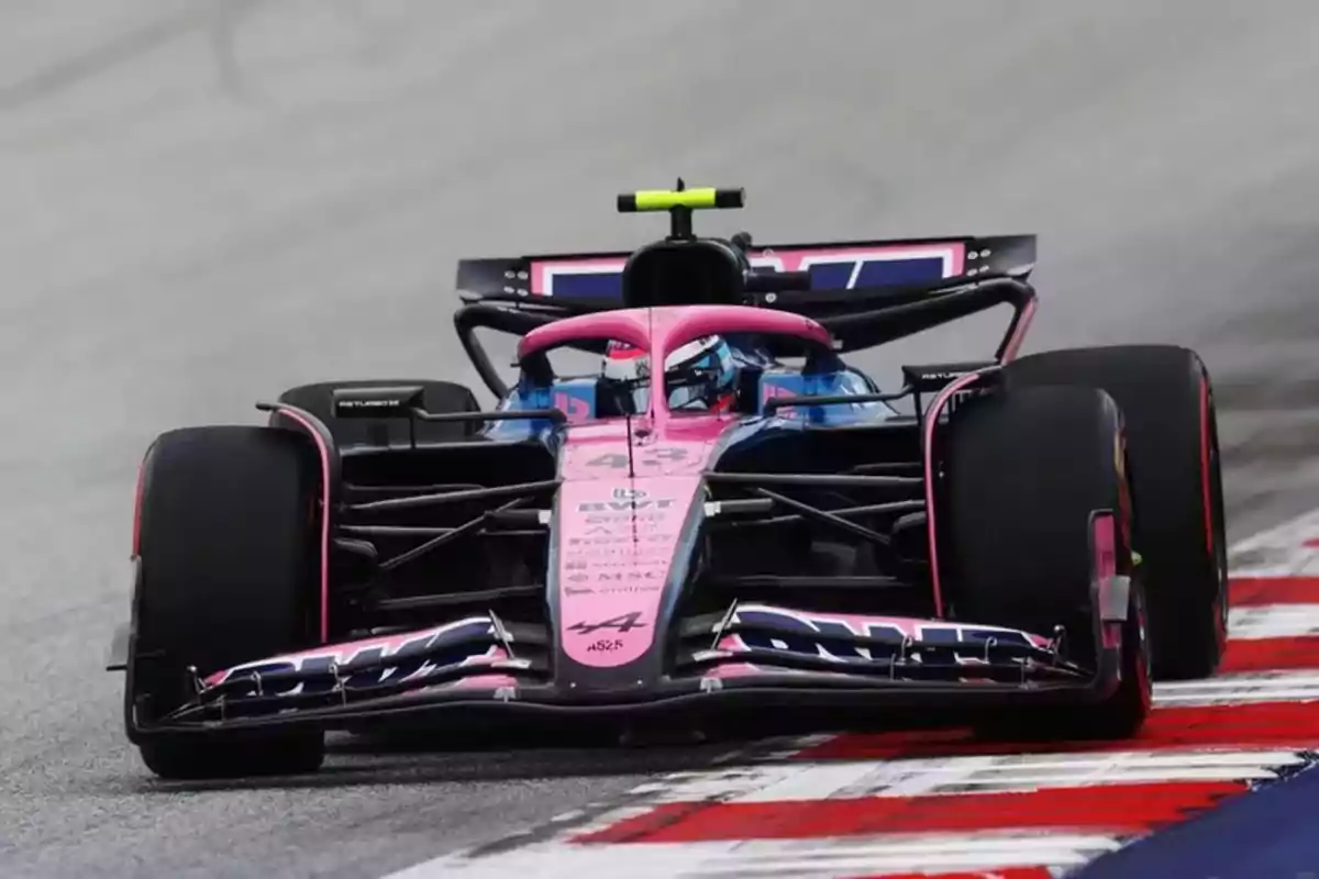 A pink and blue Formula 1 car drives on a racetrack while taking a turn. A pink and blue Formula 1 car drives on a racetrack while taking a turn.