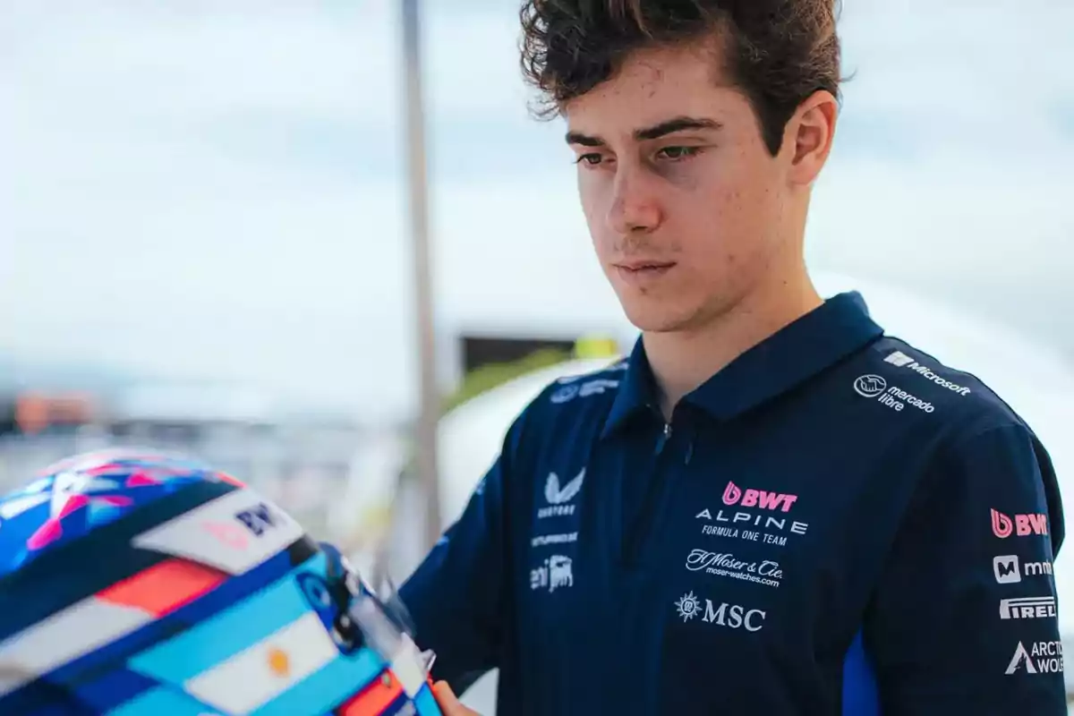 Young man in a blue motorsport team jersey looking at a colorful racing helmet