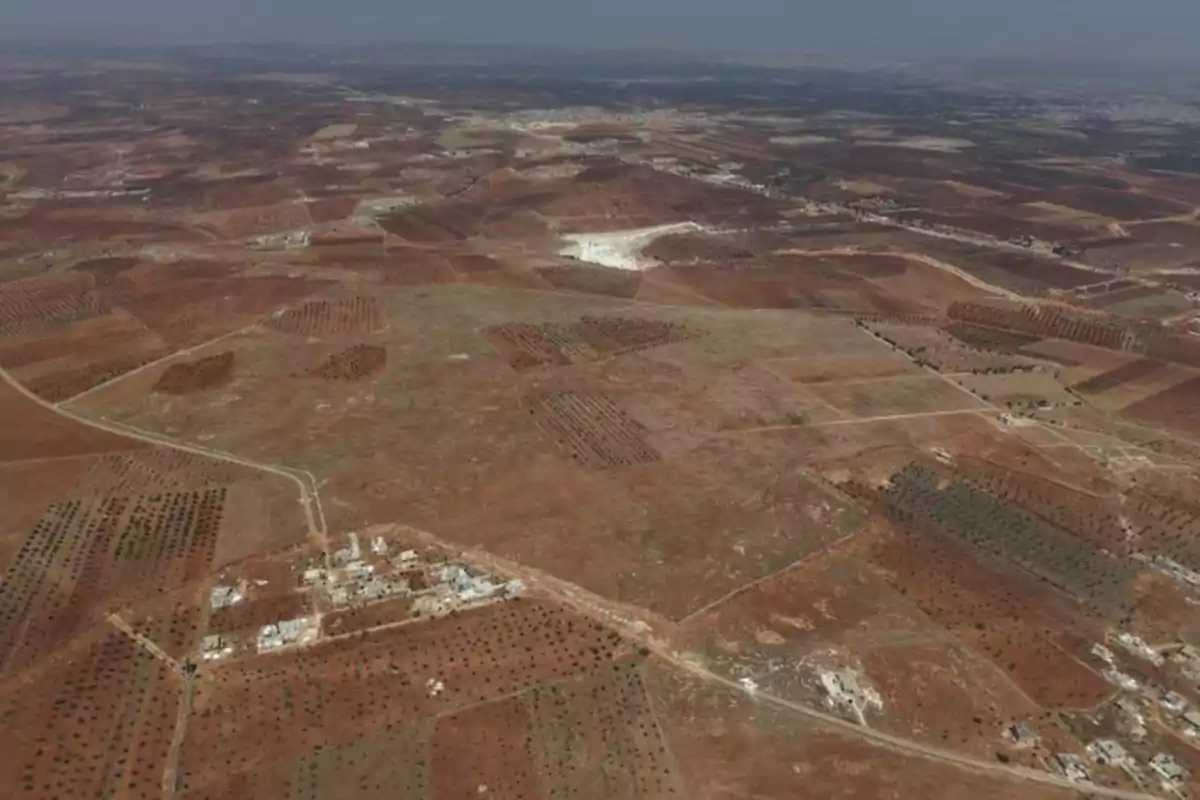 Vista aérea de un paisaje árido con campos de cultivo y algunas edificaciones dispersas Vista aérea de un paisaje árido con campos de cultivo y algunas edificaciones dispersas