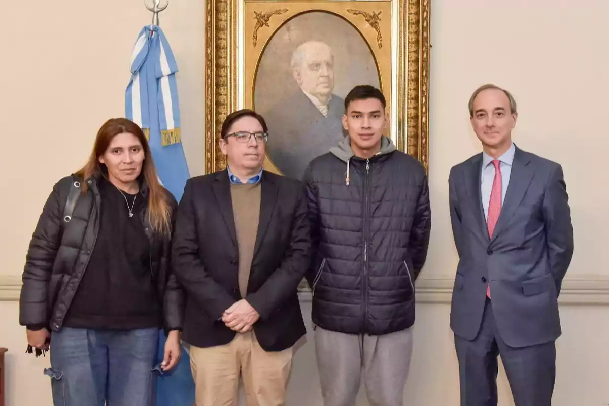 Cuatro personas posan frente a un cuadro antiguo y una bandera argentina en una sala formal