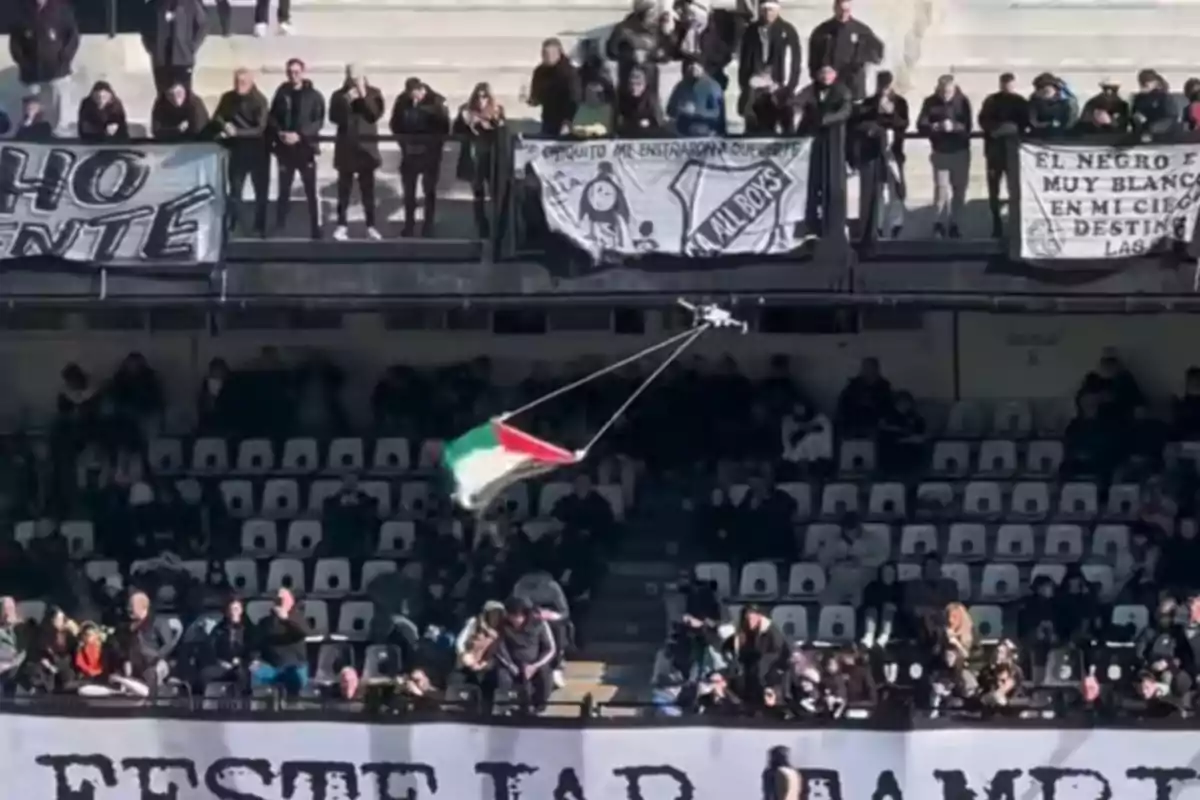 Un dron vuela sobre las gradas de un estadio llevando una bandera con los colores rojo, blanco y verde mientras los aficionados observan desde sus asientos Un dron vuela sobre las gradas de un estadio llevando una bandera con los colores rojo, blanco y verde mientras los aficionados observan desde sus asientos