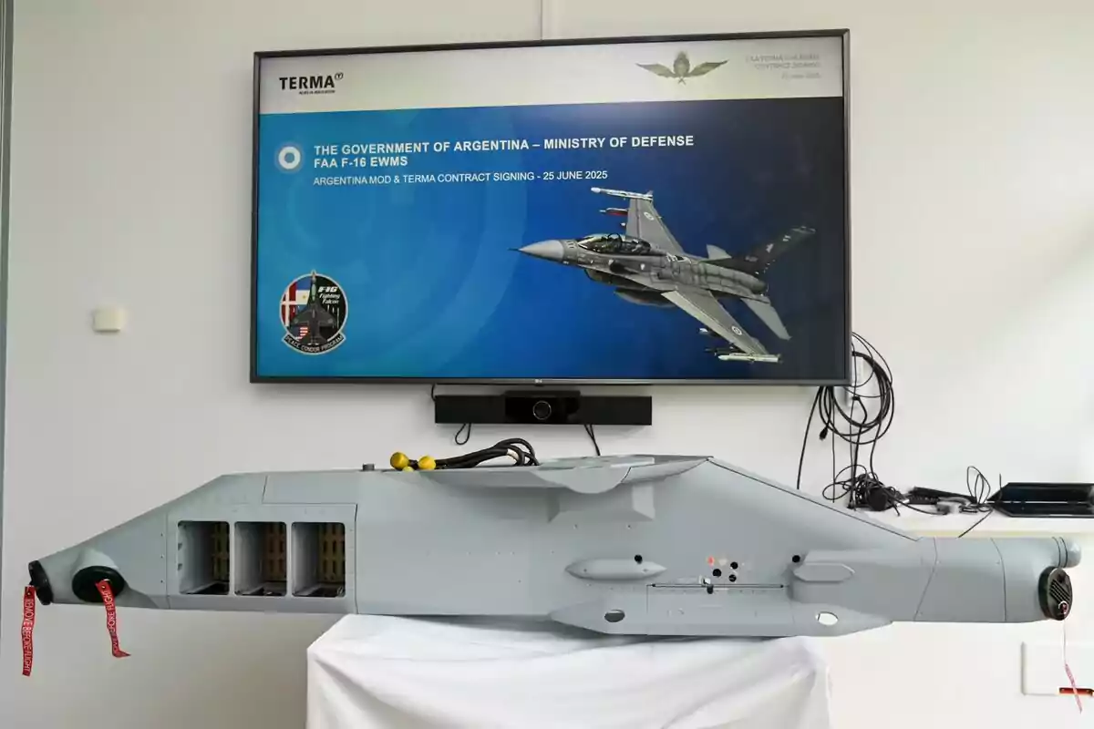 Pantalla con información sobre un contrato entre el Ministerio de Defensa de Argentina y la empresa Terma para el F-16, junto a un equipo militar expuesto sobre una mesa. Pantalla con información sobre un contrato entre el Ministerio de Defensa de Argentina y la empresa Terma para el F-16, junto a un equipo militar expuesto sobre una mesa.