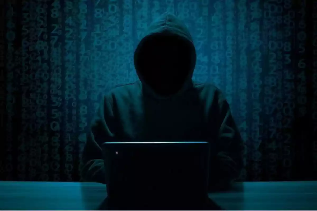 Persona encapuchada usando una computadora portátil en un entorno oscuro con números en el fondo Persona encapuchada usando una computadora portátil en un entorno oscuro con números en el fondo