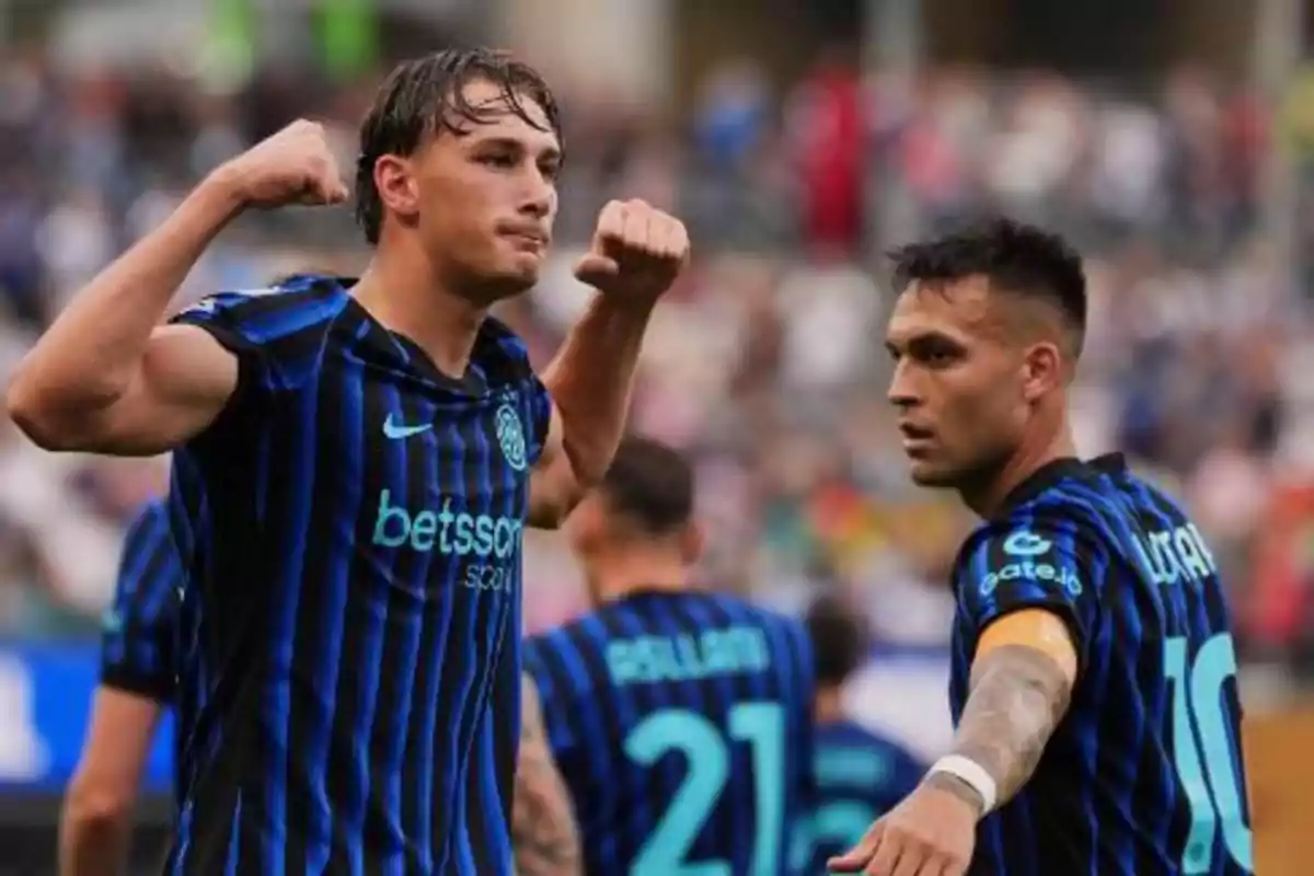 Dos futbolistas con uniforme azul y negro celebran en la cancha durante un partido