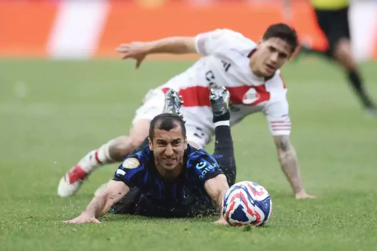 Dos futbolistas caen al césped durante un partido mientras luchan por el balón Dos futbolistas caen al césped durante un partido mientras luchan por el balón