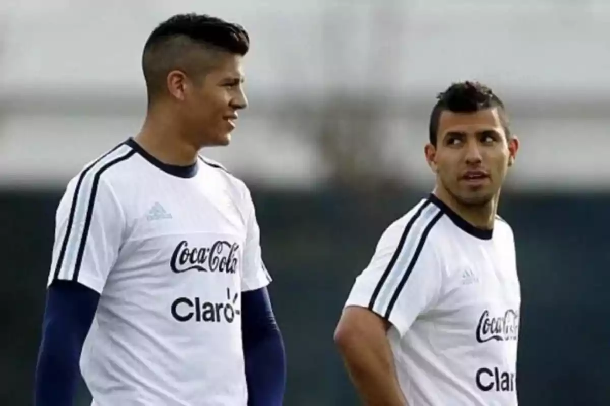 Dos futbolistas con uniforme de entrenamiento blanco conversan en una cancha al aire libre Dos futbolistas con uniforme de entrenamiento blanco conversan en una cancha al aire libre