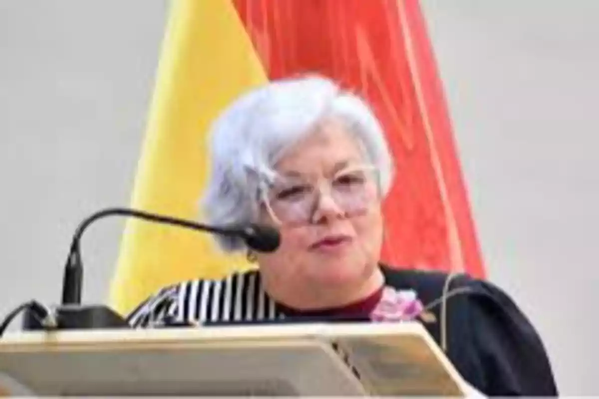 Gray-haired woman with glasses speaking at a podium with a microphone and flags in the background Gray-haired woman with glasses speaking at a podium with a microphone and flags in the background