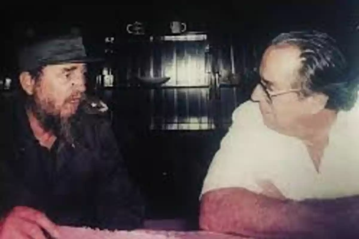 Two men sitting face to face talking at a table in a dark indoor setting