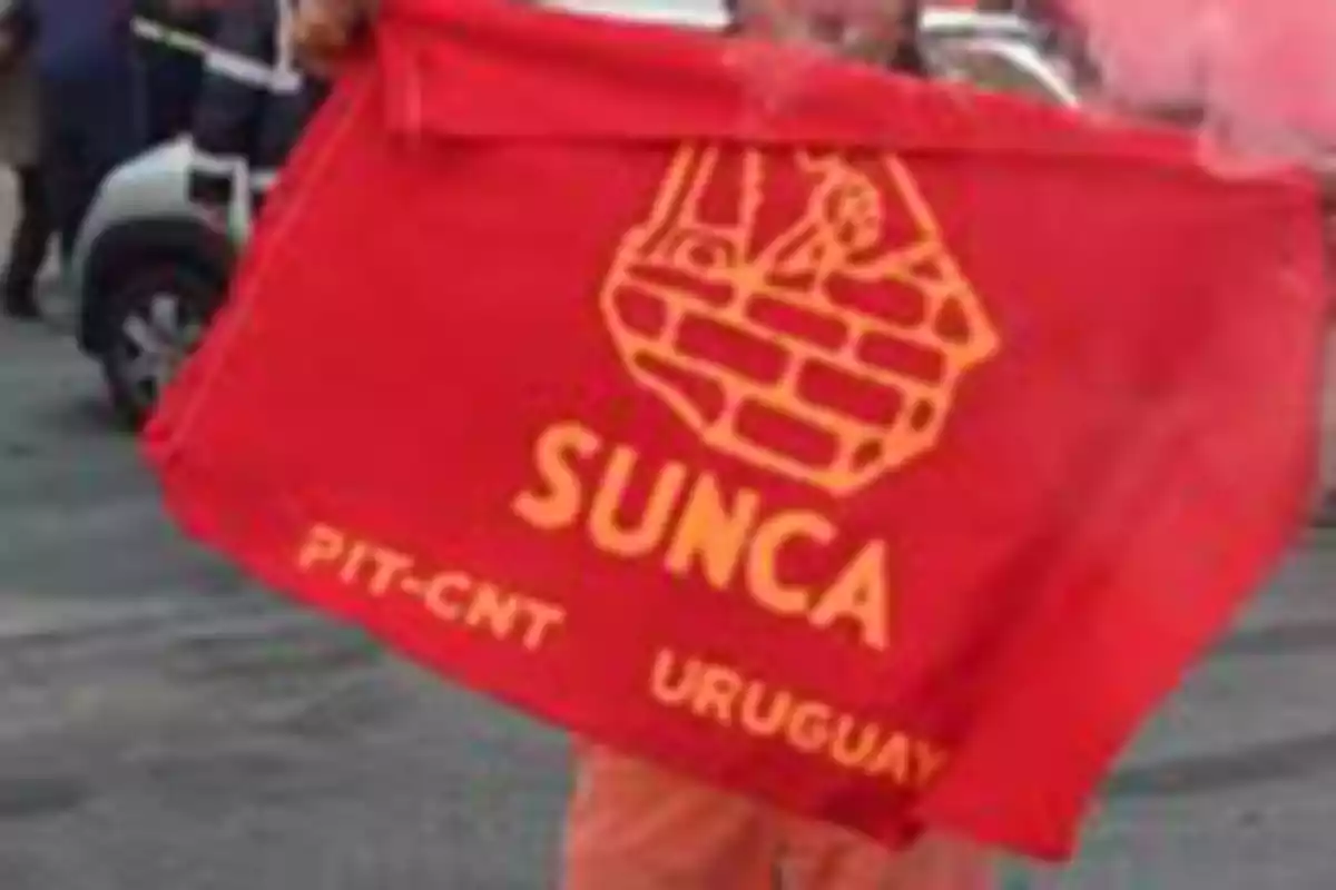 Persona sosteniendo una bandera roja del sindicato SUNCA de Uruguay en una manifestación Persona sosteniendo una bandera roja del sindicato SUNCA de Uruguay en una manifestación