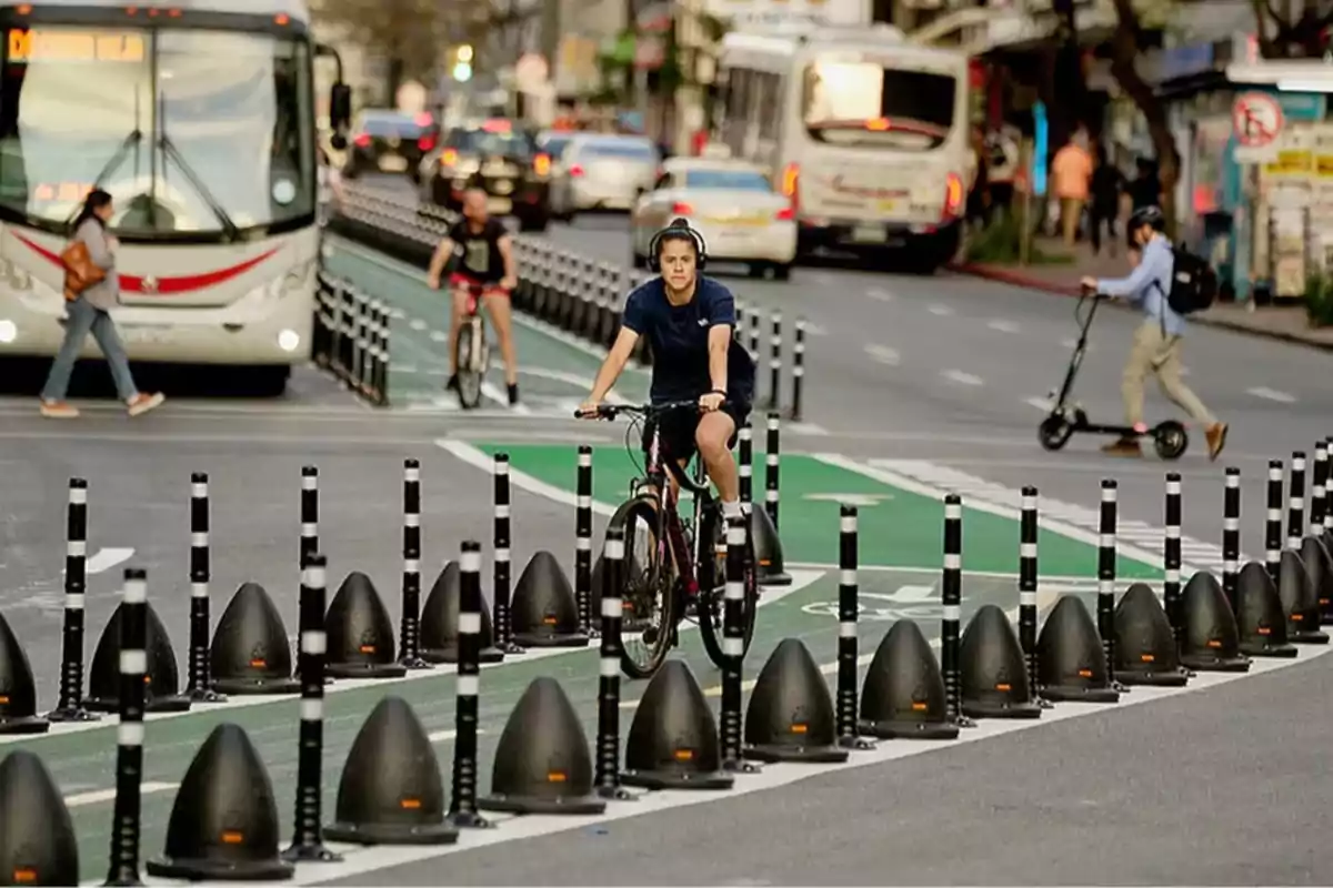 Person riding a bicycle on a protected bike lane on a busy avenue with pedestrians, scooters, and buses in the background Person riding a bicycle on a protected bike lane on a busy avenue with pedestrians, scooters, and buses in the background