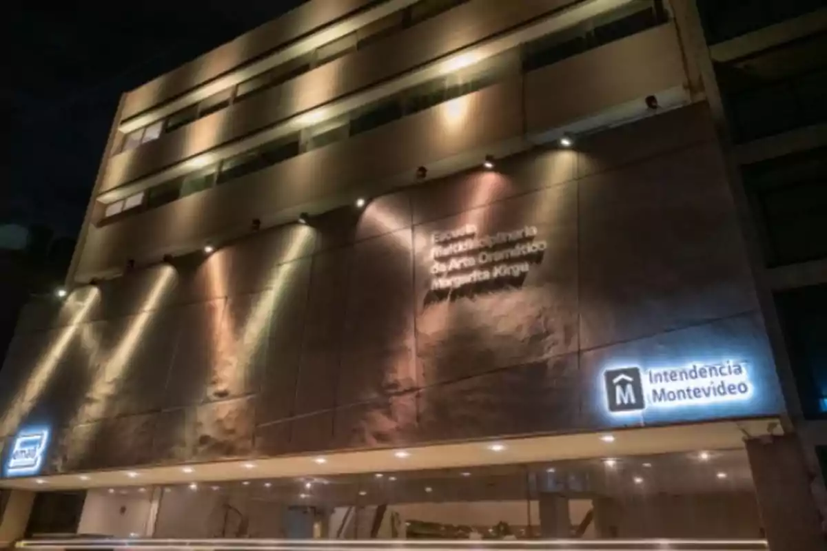 Illuminated facade of a modern building with signs for the Montevideo City Hall and the Margarita Xirgu Multidisciplinary School of Dramatic Art