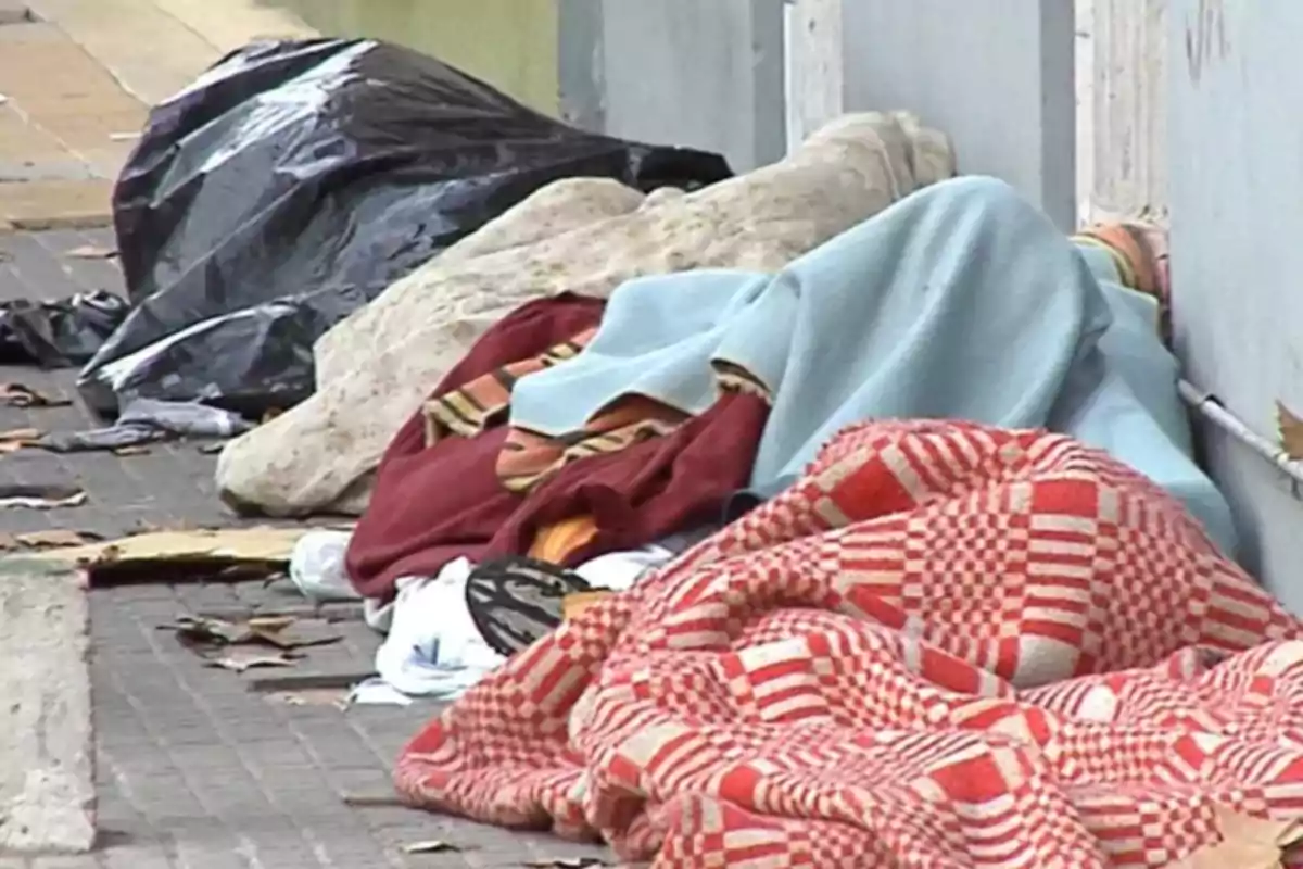 People sleeping on the street covered with blankets of different colors on the sidewalk