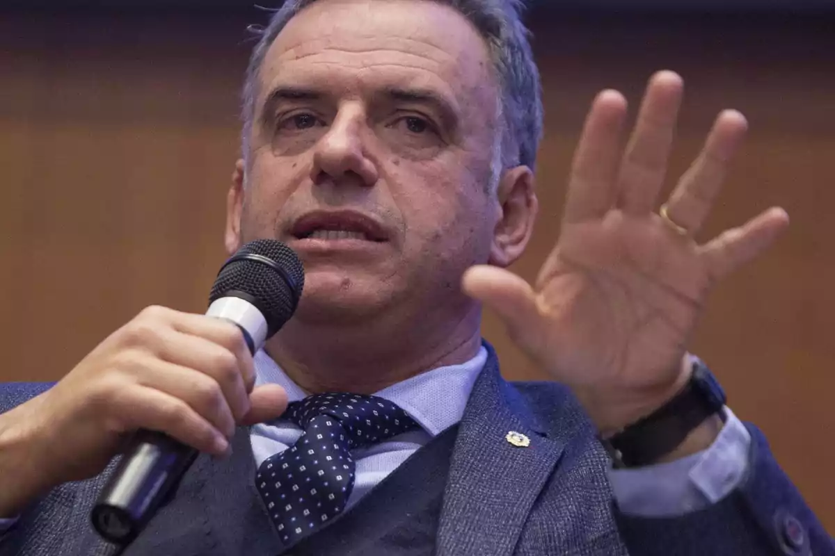 Middle-aged man in a blue suit speaking in public while holding a microphone and raising his hand Middle-aged man in a blue suit speaking in public while holding a microphone and raising his hand