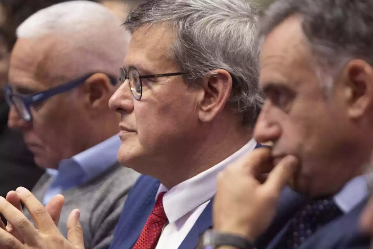Three middle-aged men sitting in a row paying attention to an event or conference.