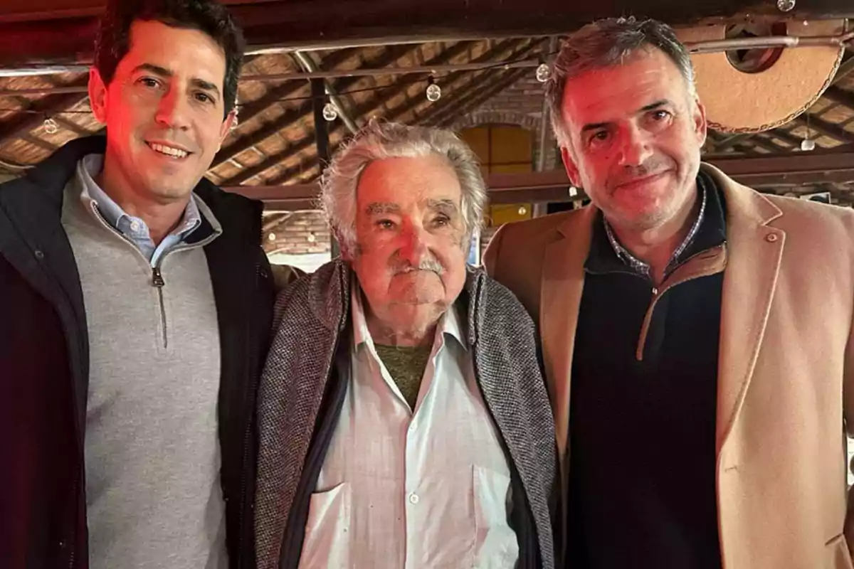 Tres hombres posan juntos y sonríen en un ambiente interior con techo de madera