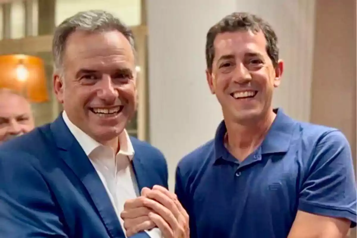 Dos hombres sonrientes se saludan estrechando las manos en un ambiente interior iluminado Dos hombres sonrientes se saludan estrechando las manos en un ambiente interior iluminado