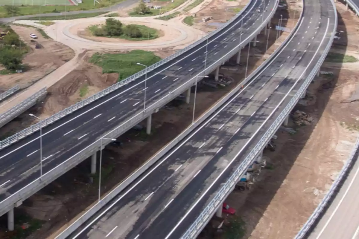 Vista aérea de un distribuidor vial con varios carriles elevados y un entorno en construcción