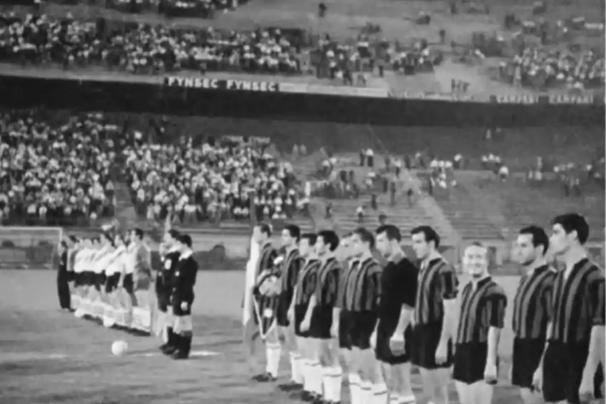 Dos equipos de fútbol alineados en el campo antes de comenzar un partido en un estadio con público en las gradas Dos equipos de fútbol alineados en el campo antes de comenzar un partido en un estadio con público en las gradas