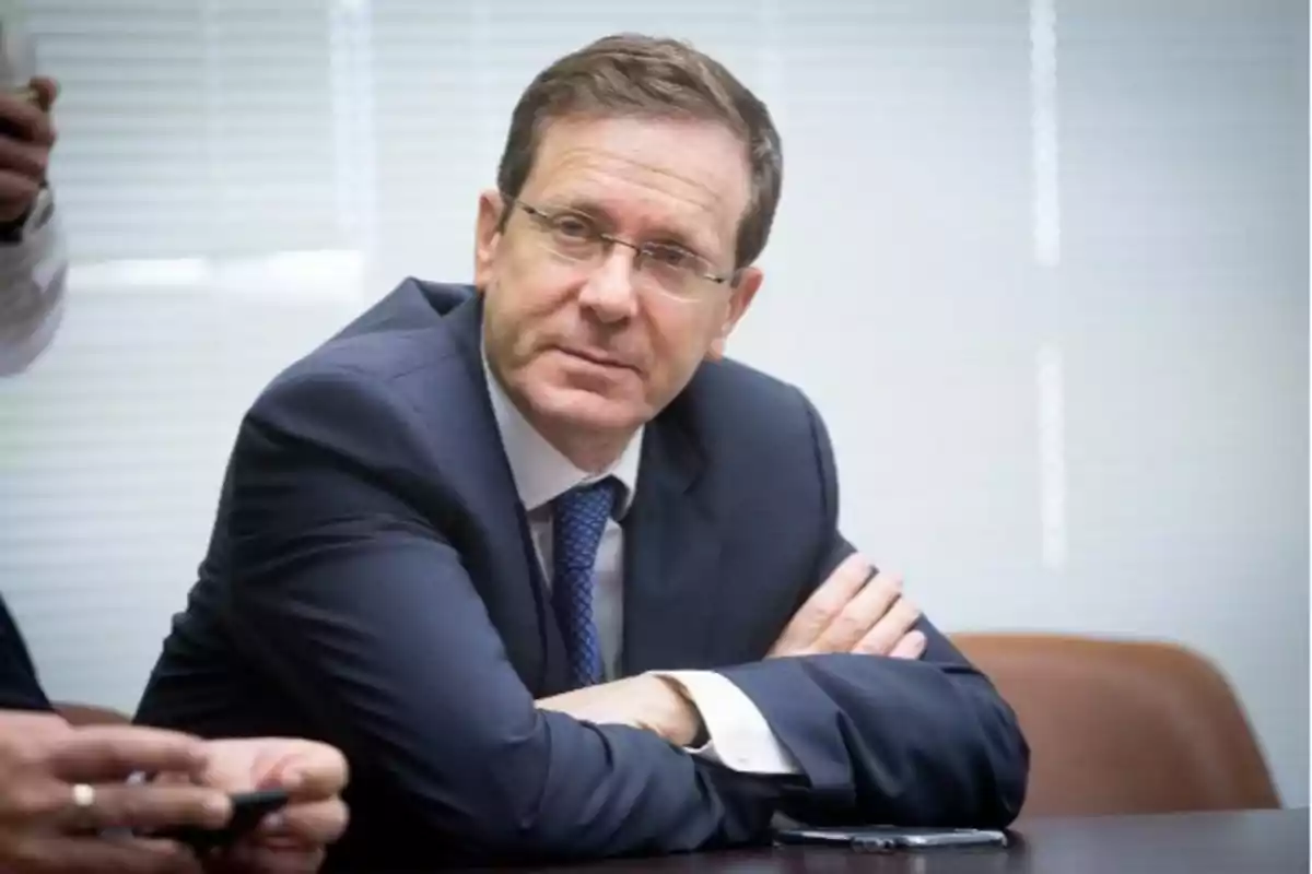 Hombre de mediana edad con gafas y traje azul sentado en una mesa mirando hacia la cámara Hombre de mediana edad con gafas y traje azul sentado en una mesa mirando hacia la cámara