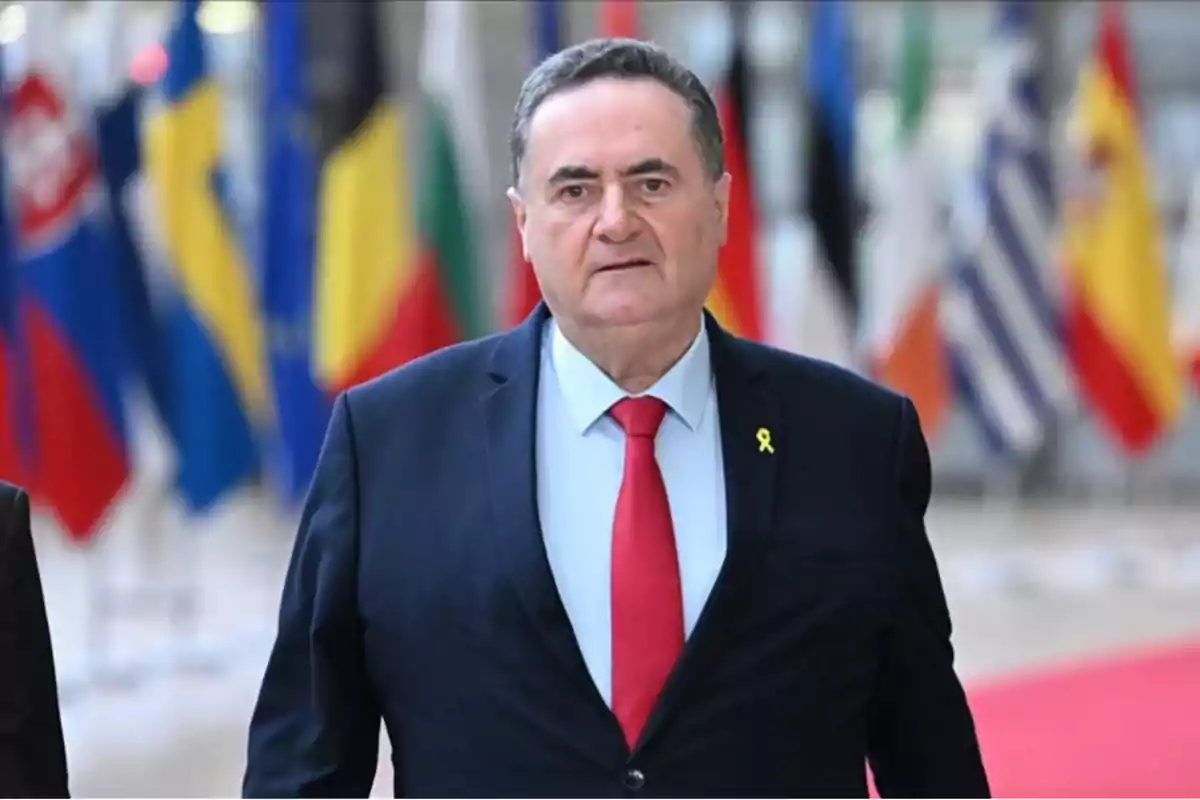 Man in a dark suit and red tie walking at an official event with flags of several countries in the background Man in a dark suit and red tie walking at an official event with flags of several countries in the background