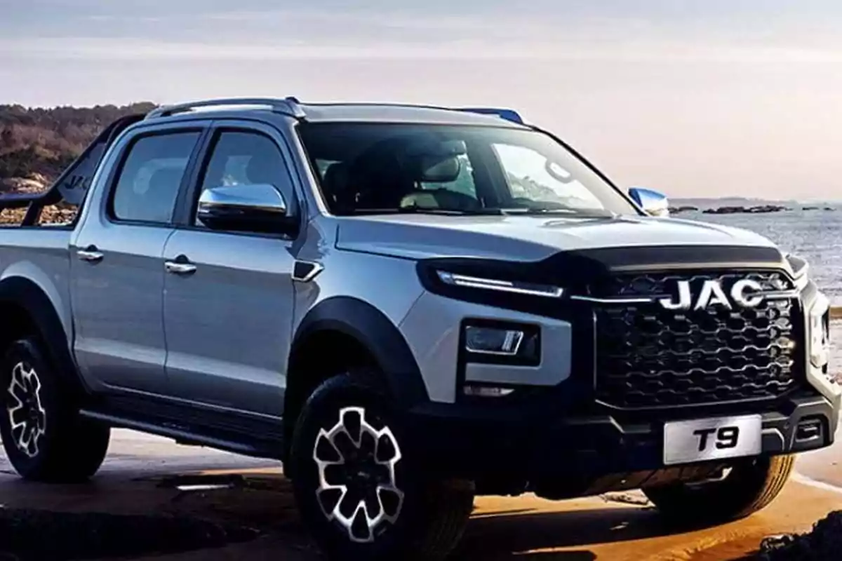 Camioneta JAC T9 color gris estacionada cerca de la playa con el mar y colinas al fondo
