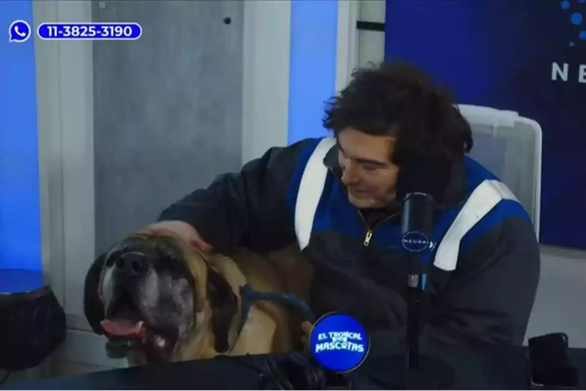 Un hombre acaricia a un perro grande durante un programa de radio llamado El Tropical Mascotas, con un micrófono y un número de WhatsApp visibles en la imagen.