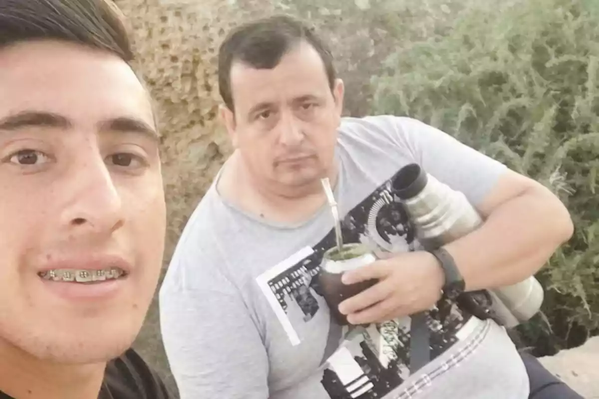 Dos personas al aire libre, una de ellas sostiene un mate y un termo mientras la otra sonríe hacia la cámara