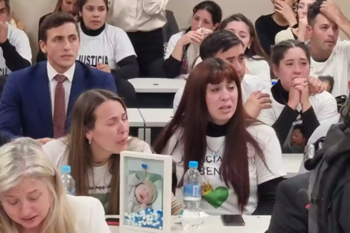 Personas llorando y mostrando dolor en una sala mientras sostienen una foto de un bebé