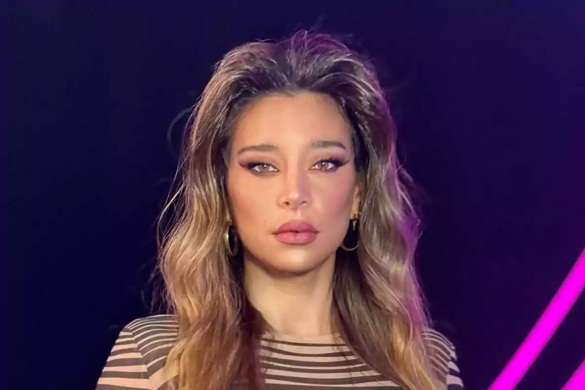 Long, wavy-haired woman with striking makeup and a dark background with pink neon lights