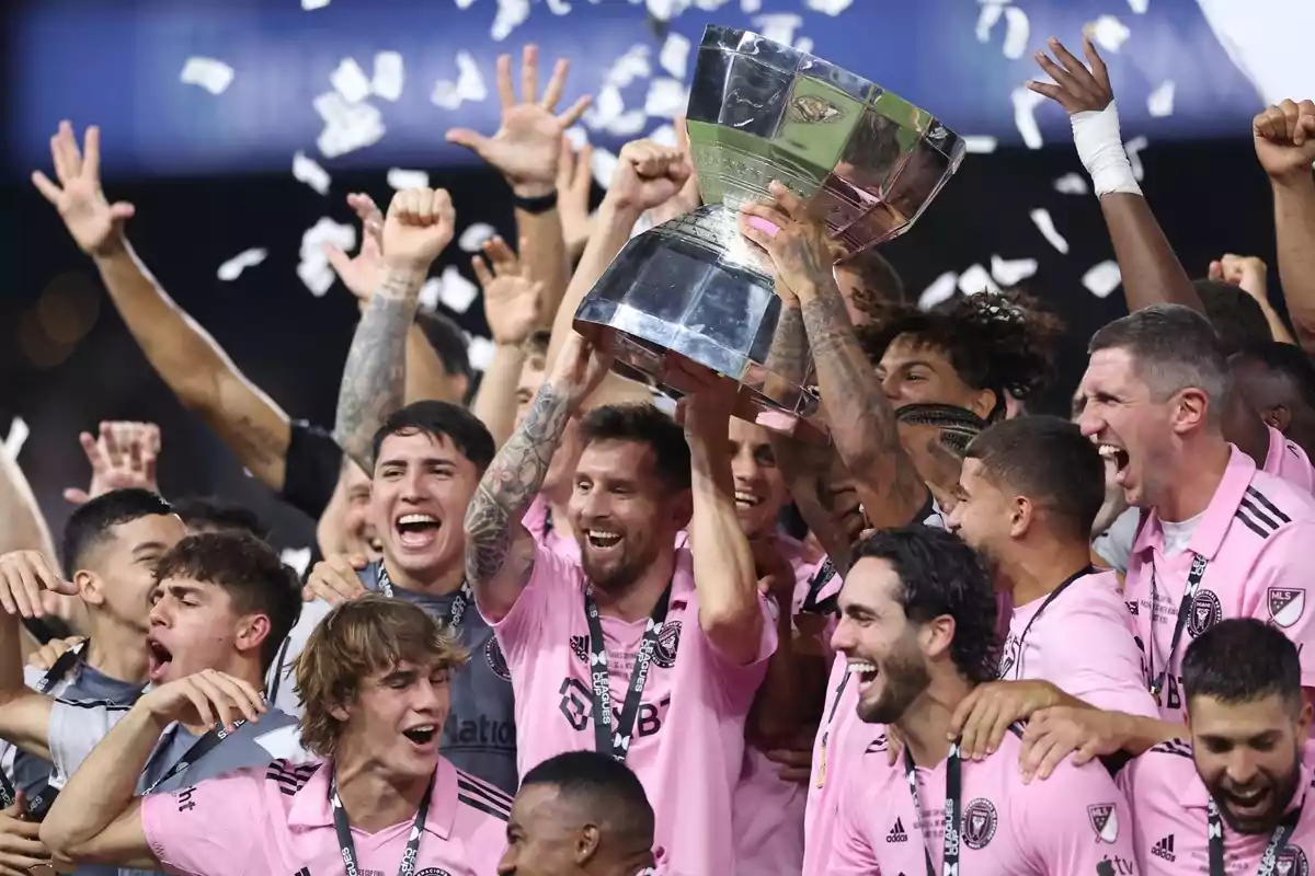 Jugadores de un equipo de fútbol con uniforme rosa celebran levantando un trofeo rodeados de confeti y sonrisas Jugadores de un equipo de fútbol con uniforme rosa celebran levantando un trofeo rodeados de confeti y sonrisas